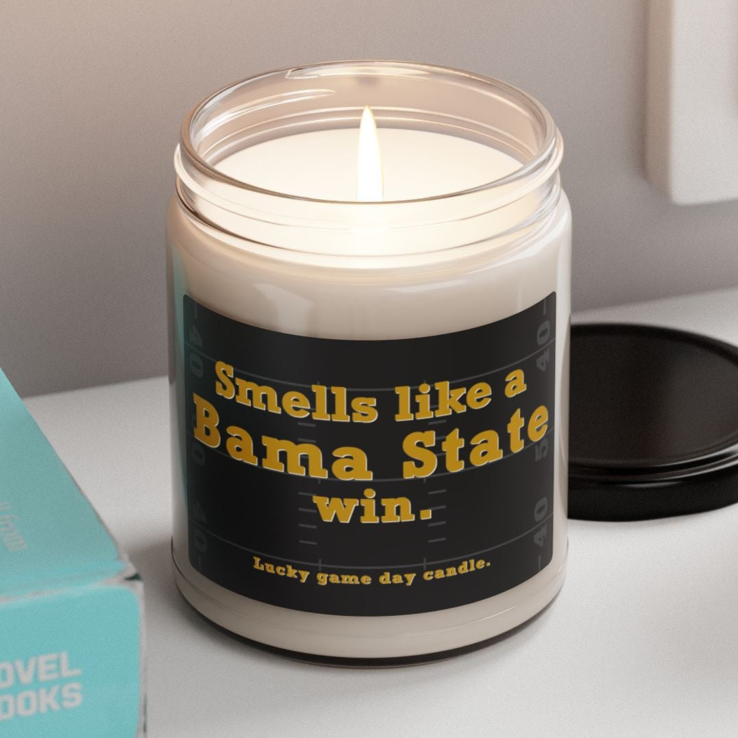 Alabama State candle with a humorous label on a shelf next to books and a plant