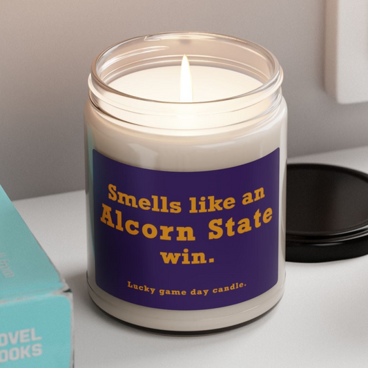 Candle with a humorous label on a shelf next to books and a plant
