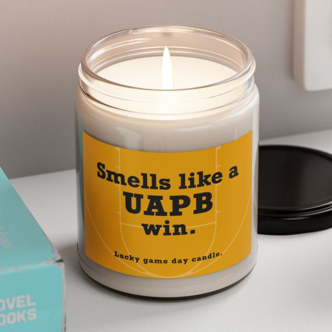 Arkansas Pine-Bluff candle with a humorous label on a shelf with books and a plant