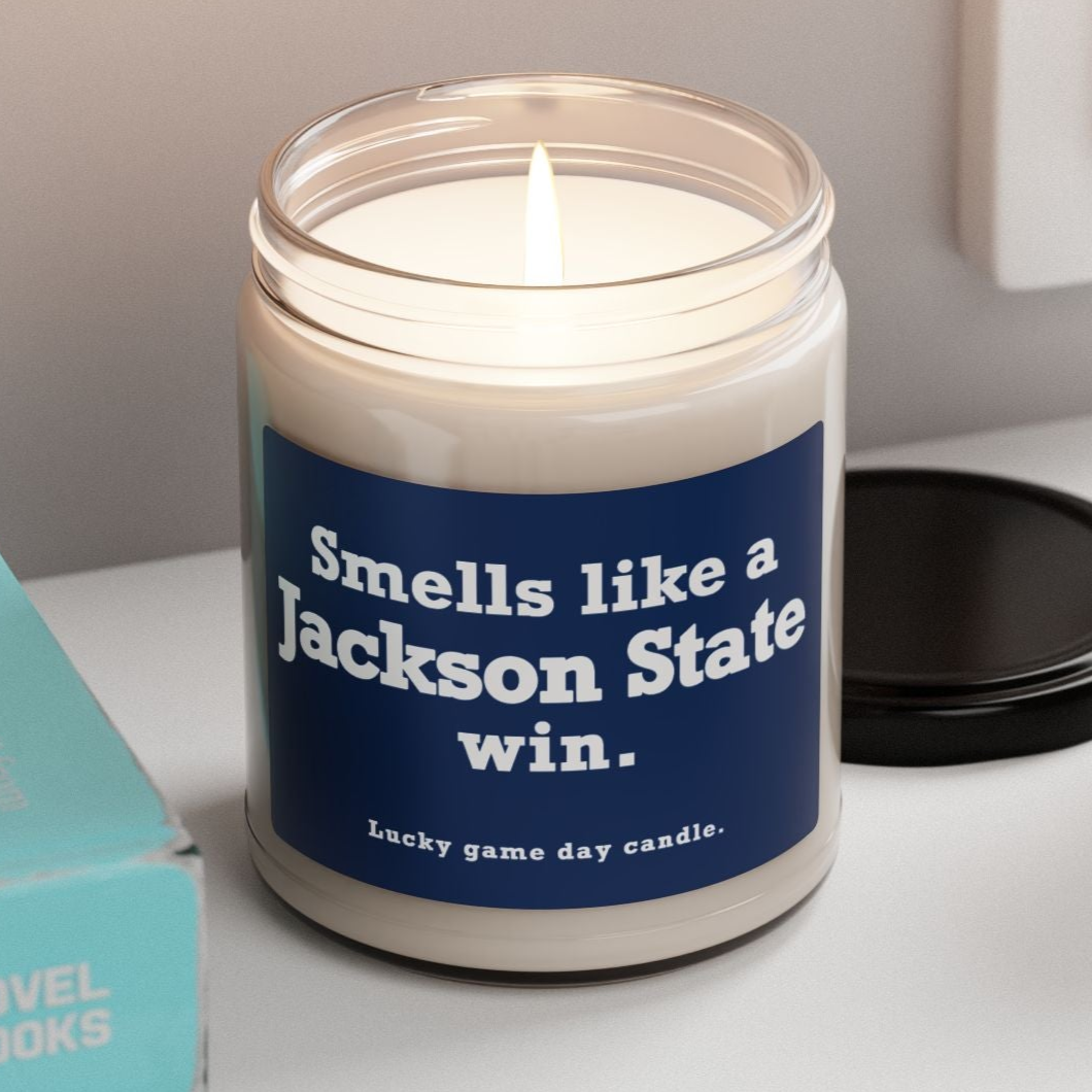 Jackson State candle with a blue label on a shelf next to books and a plant