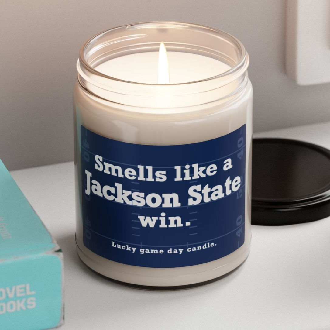 Jackson State candle with a blue label on a shelf next to books and a plant