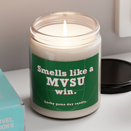 MVSU candle with a humorous label on a shelf next to books and a plant