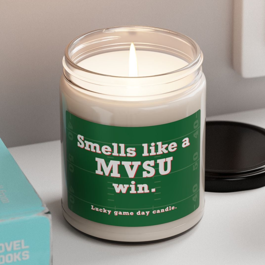 MVSU candle with a humorous label on a shelf next to books and a plant
