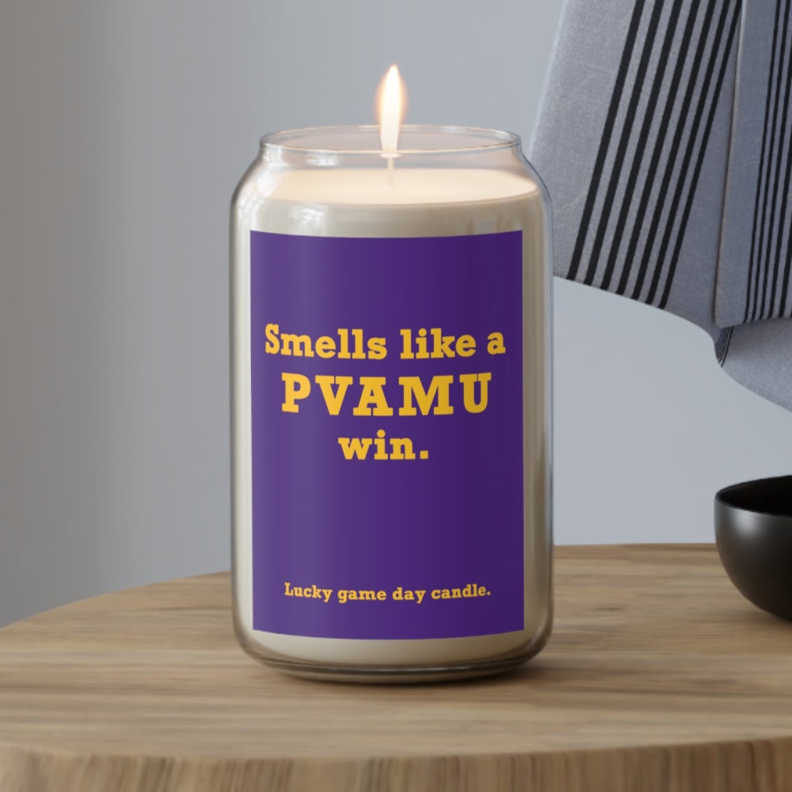 Prairie View A&M candle with a purple label on a wooden table, featuring text.