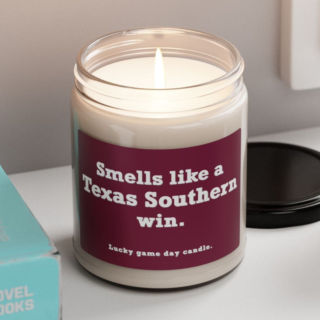 Texas Southern candle with a purple label on a shelf next to books and a plant